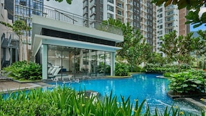 A modern pool area with a glass-enclosed lounge, surrounded by lush greenery and tall residential buildings in the background. - SCAPES Hotel (Genting Highlands)