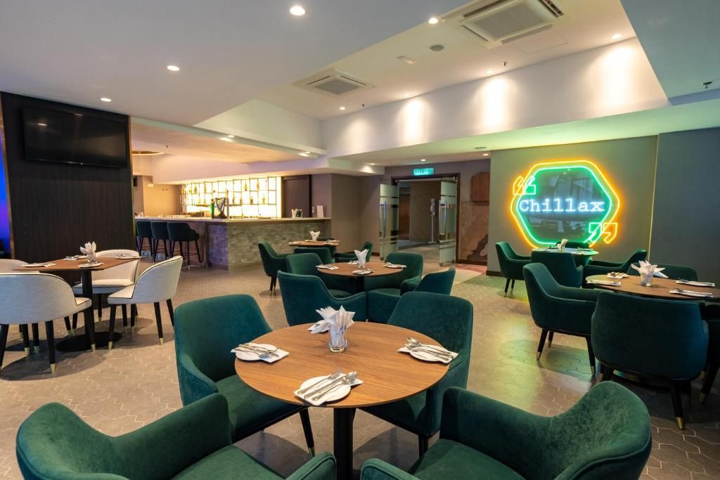 Een restaurant met ronde tafels en groene stoelen, een neonreclame en een bar.