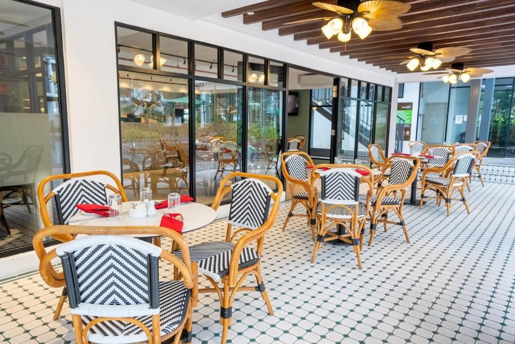 A restaurant with wicker chairs and tables, large windows, and a tiled floor.