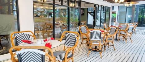 Un restaurante con sillas y mesas de mimbre, ventanas amplias y suelo de baldosas.
