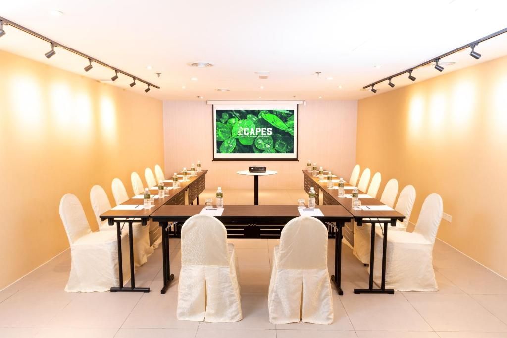 Un salón de conferencias con una larga mesa, sillas, una pantalla y un proyector.
