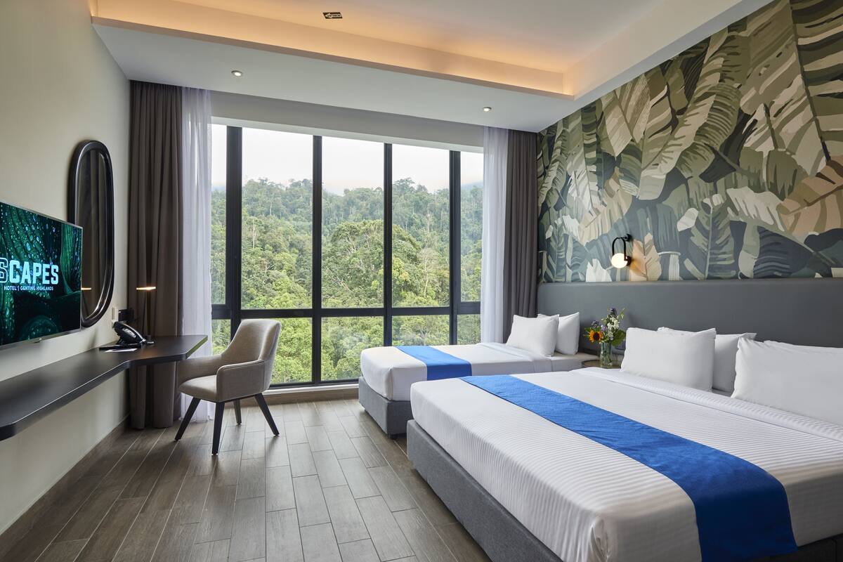 Habitación de hotel con dos camas, un escritorio, un televisor y un ventanal con vistas al bosque.