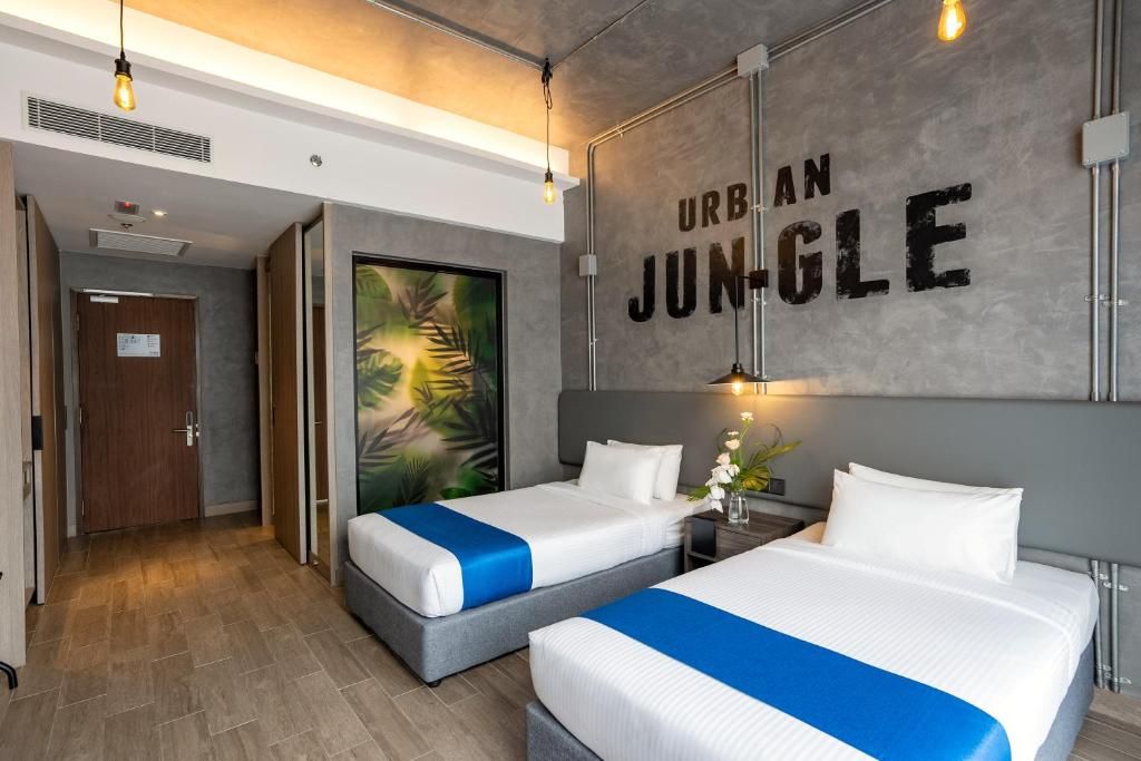 A hotel room with two beds, a large painting, and a wall with 'URBAN JUNGLE' text.