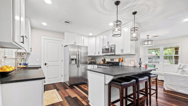 A modern kitchen with white cabinets, stainless steel appliances, a central island with stools, and a large window providing natural light. - the ORANGE DOOR just steps from art, trails & dining (Bentonville)