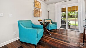 A room with two teal chairs, a wooden floor, a chandelier, and a view of the outdoors through large glass doors. - the ORANGE DOOR just steps from art, trails & dining (Bentonville)