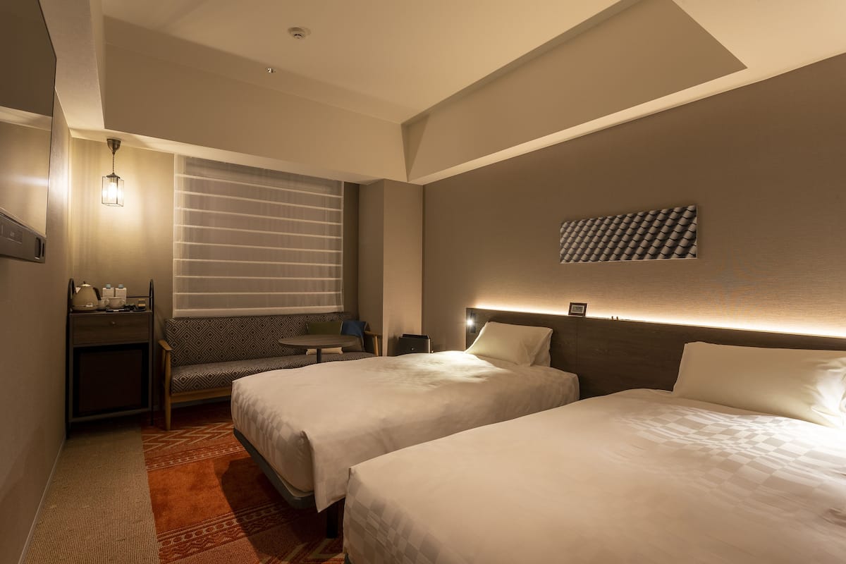 Une chambre d’hôtel avec deux lits, un bureau, une chaise et un téléviseur.