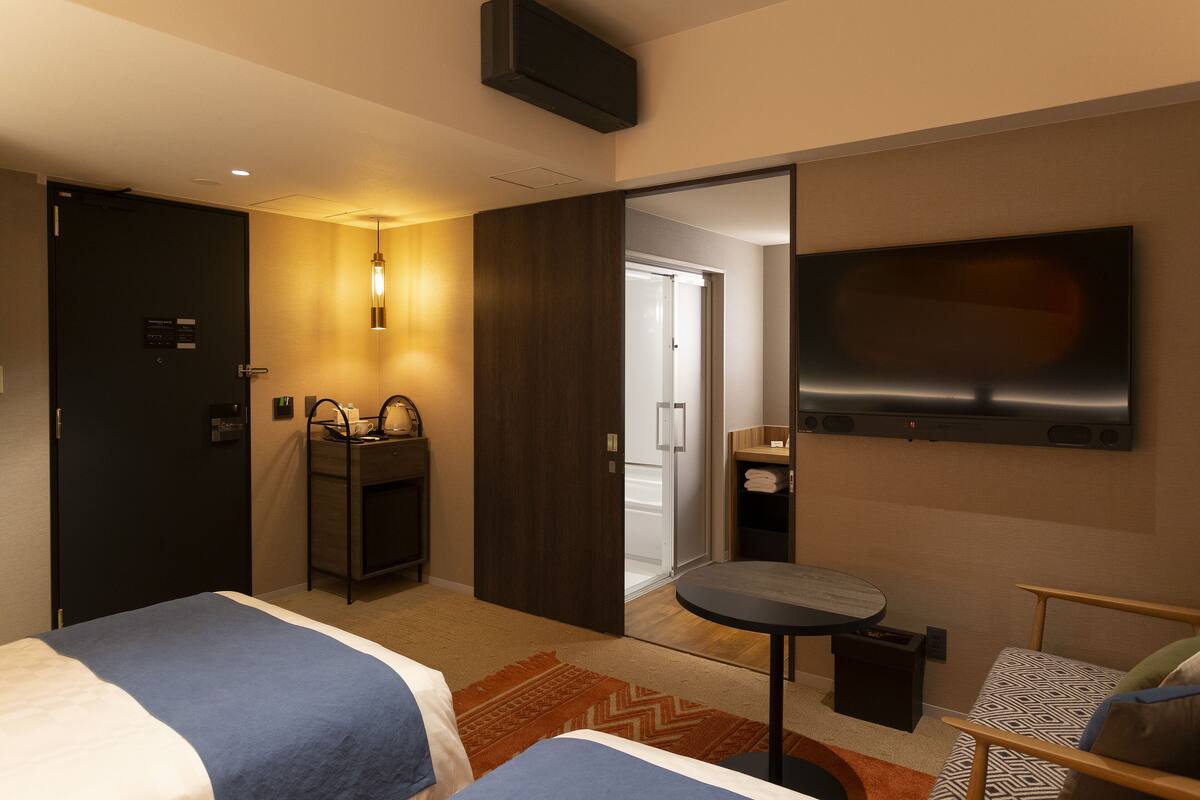 Une chambre d’hôtel avec deux lits, une petite table, un téléviseur, un bureau avec une chaise et un miroir.
