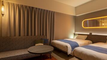 A hotel room with a sofa, two single beds, a small round table, and a mirror with a light.