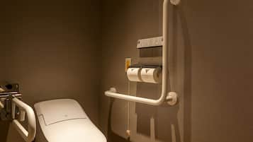 A bathroom with a toilet, a handrail, and a wall-mounted toilet paper holder.