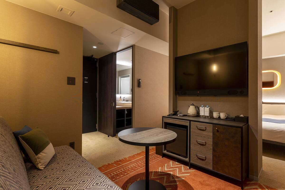 Une chambre d’hôtel avec un canapé, une petite table ronde, un minibar, une télévision et un lit.