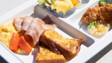 Bandeja de desayuno con tostadas, jamón, huevos revueltos y una guarnición de frutas y verduras.