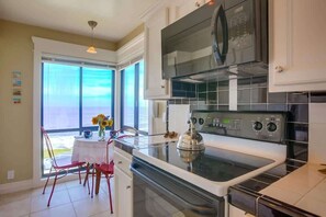 A kitchen with a stove, oven, and microwave, a dining table with chairs, and a window with a view. - Perfect Sunsets - Unobstructed views of the ocean (La Jolla)