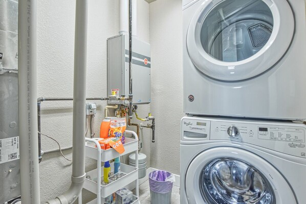 A laundry room with stacked washers and dryers, a utility cart with cleaning supplies, and a water heater.
