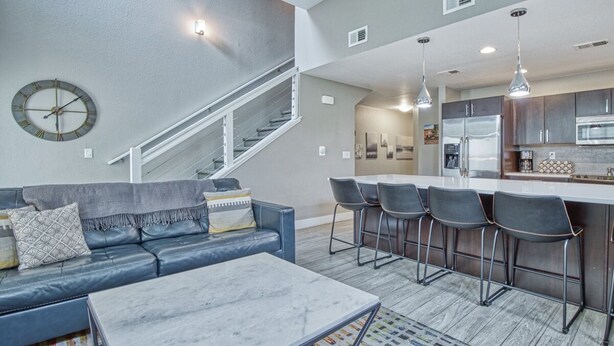A modern living room with a sofa, coffee table, and a staircase leading to a kitchen area with bar stools. - Wonderful Three Bedroom Townhome in Old Town North (Fort Collins)