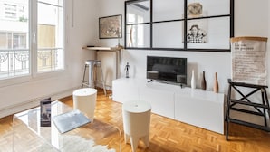 En moderne stue med et stort vindue, en hvid sofa, et fjernsyn og et lille bord.