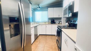 Una cocina moderna con electrodomésticos de acero inoxidable, armarios blancos y piso de baldosas.