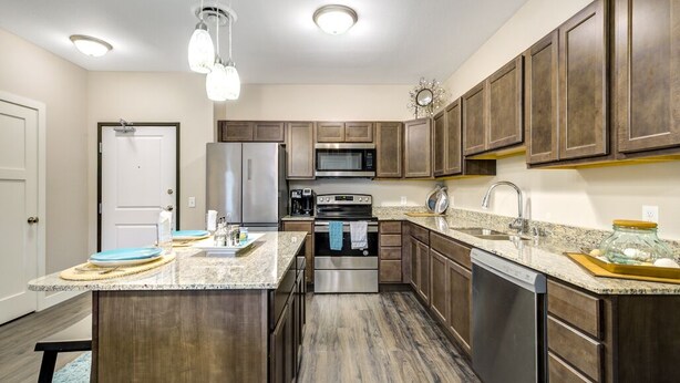 A modern kitchen with dark wood cabinets, stainless steel appliances, and a granite countertop. - Clubhouse Fully Equipped Apartment (Mankato)