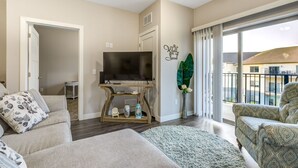 A living room with a TV, sofas, a coffee table, and a large window with a view. - Clubhouse Fully Equipped Apartment (Mankato)