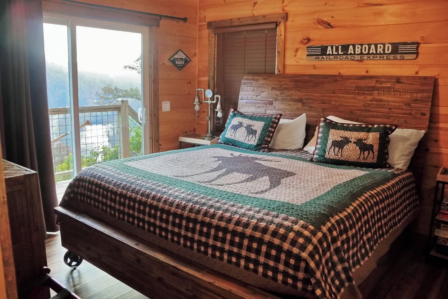A wooden cabin bedroom with a large bed, a window with a view, and a sign that reads "ALL ABOARD RAILROAD EXPRESS".