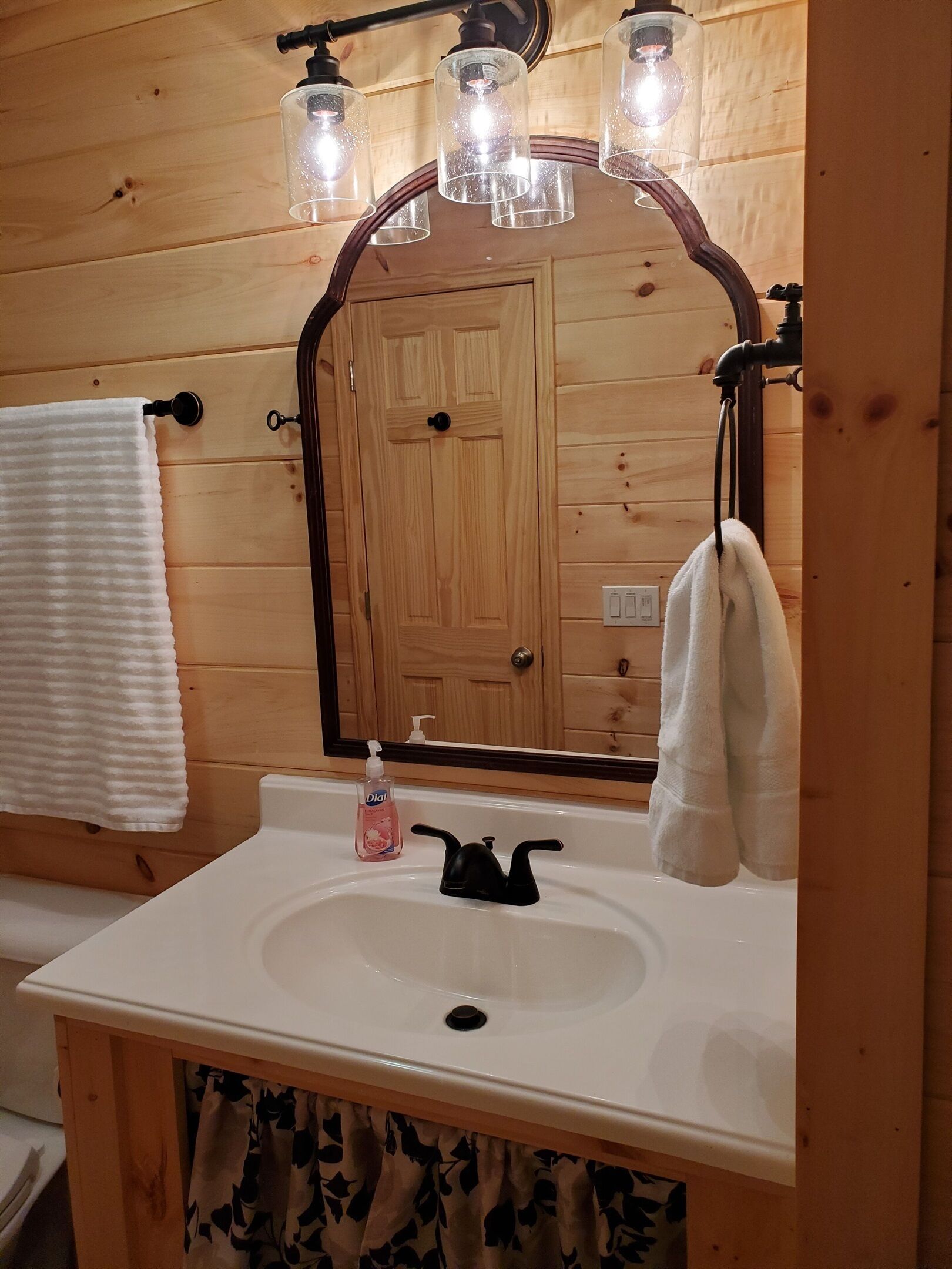 A wooden cabin bathroom with a white sink, a mirror, and a towel rack.