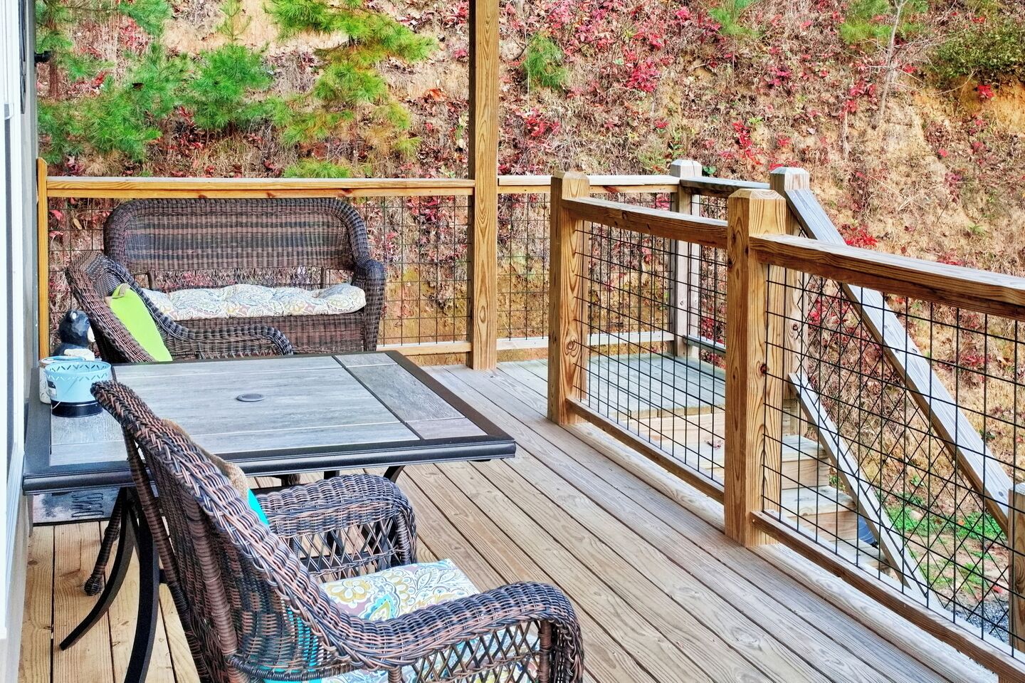 A wooden deck with wicker furniture, including a table and two chairs, and a metal railing.