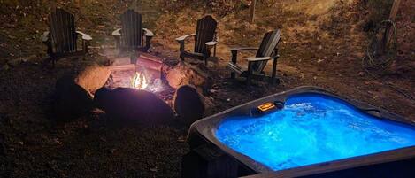 An outdoor hot tub area with a fire pit and Adirondack chairs.