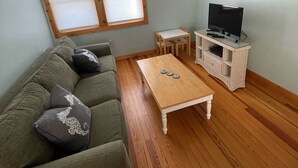 Una sala de estar con un sofá verde, una mesa de centro de madera, un televisor sobre un mueble bajo y una ventana con persianas.