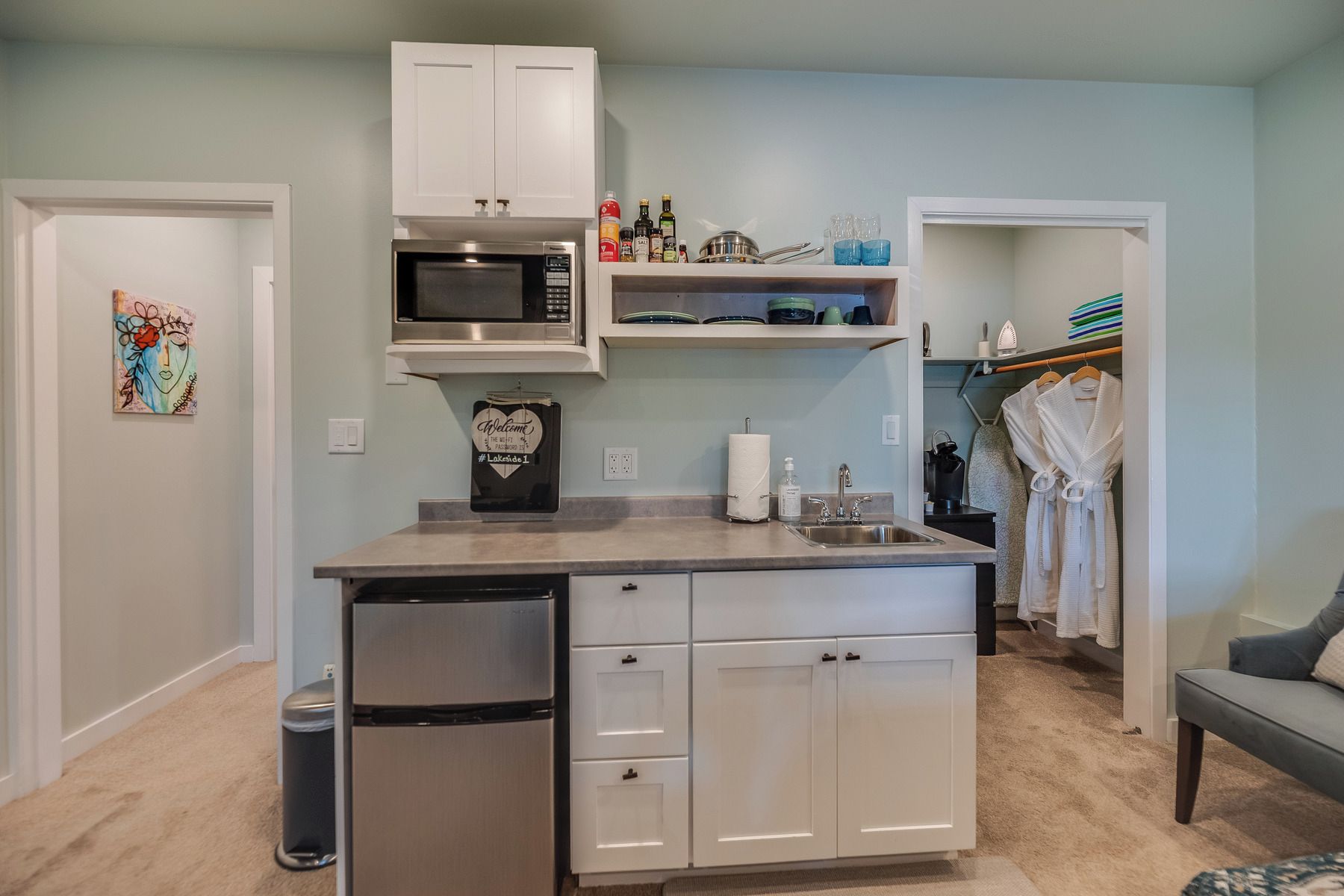 A compact kitchen with a built-in microwave, a refrigerator, and a sink. There is a small countertop with a coffee maker and a bottle of hand soap.