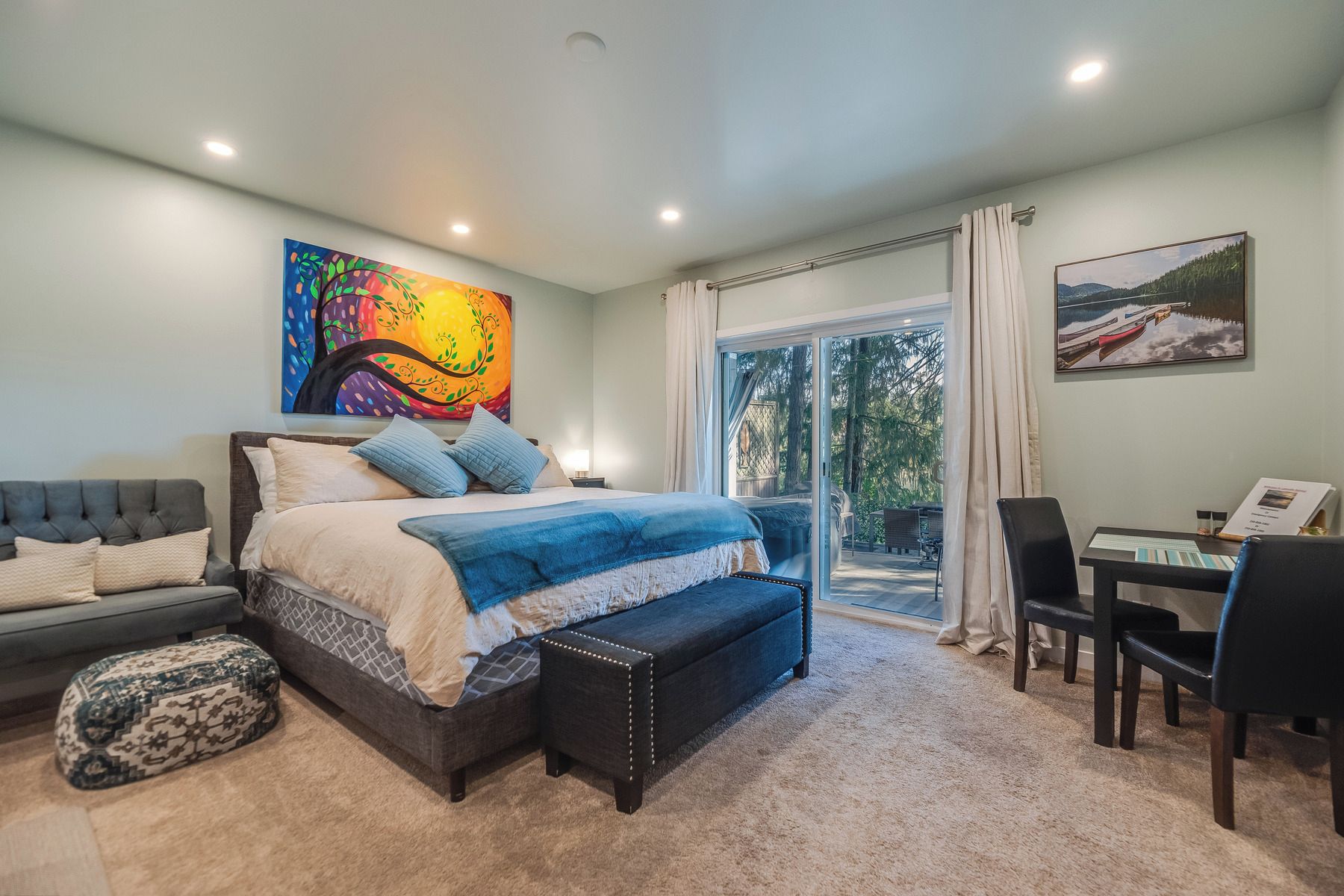 A bedroom with a bed, a bench, a desk, and chairs.