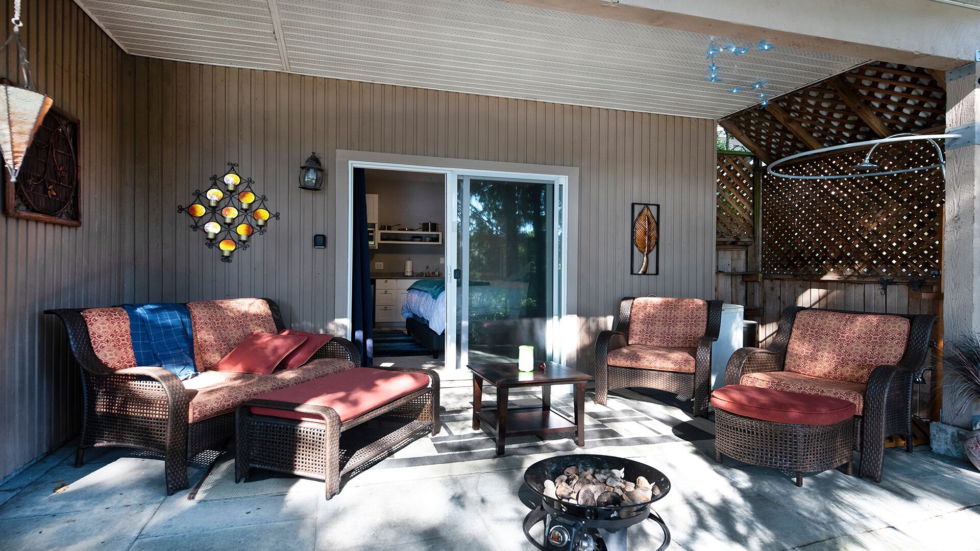 Une terrasse couverte, aménagée avec des meubles en osier, un foyer extérieur et une vue sur l’intérieur de la maison.