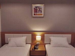 Ein Hotelzimmer mit zwei Betten, einem Nachttisch mit Lampe und einem gerahmten Bild an der Wand.