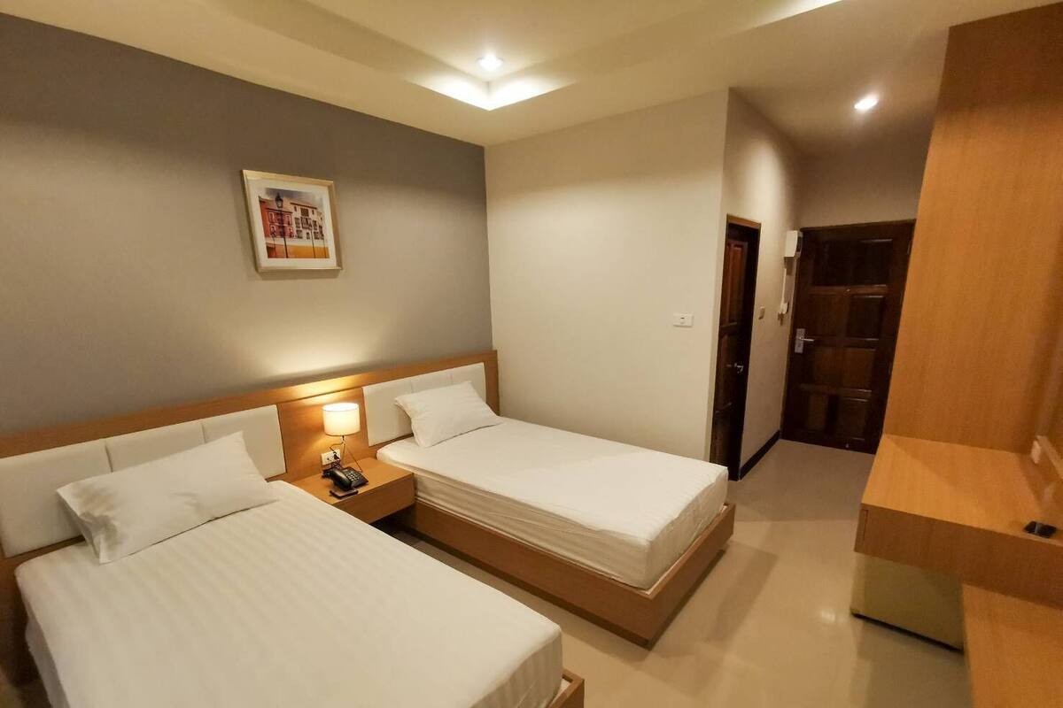 A hotel room with two beds, a nightstand with a lamp, a wooden desk, and a door leading to another room.