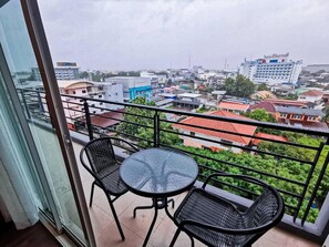Ein Balkon mit zwei Stühlen und einem Tisch, mit Blick auf eine Stadtlandschaft mit verschiedenen Gebäuden und einem großen Hotel.