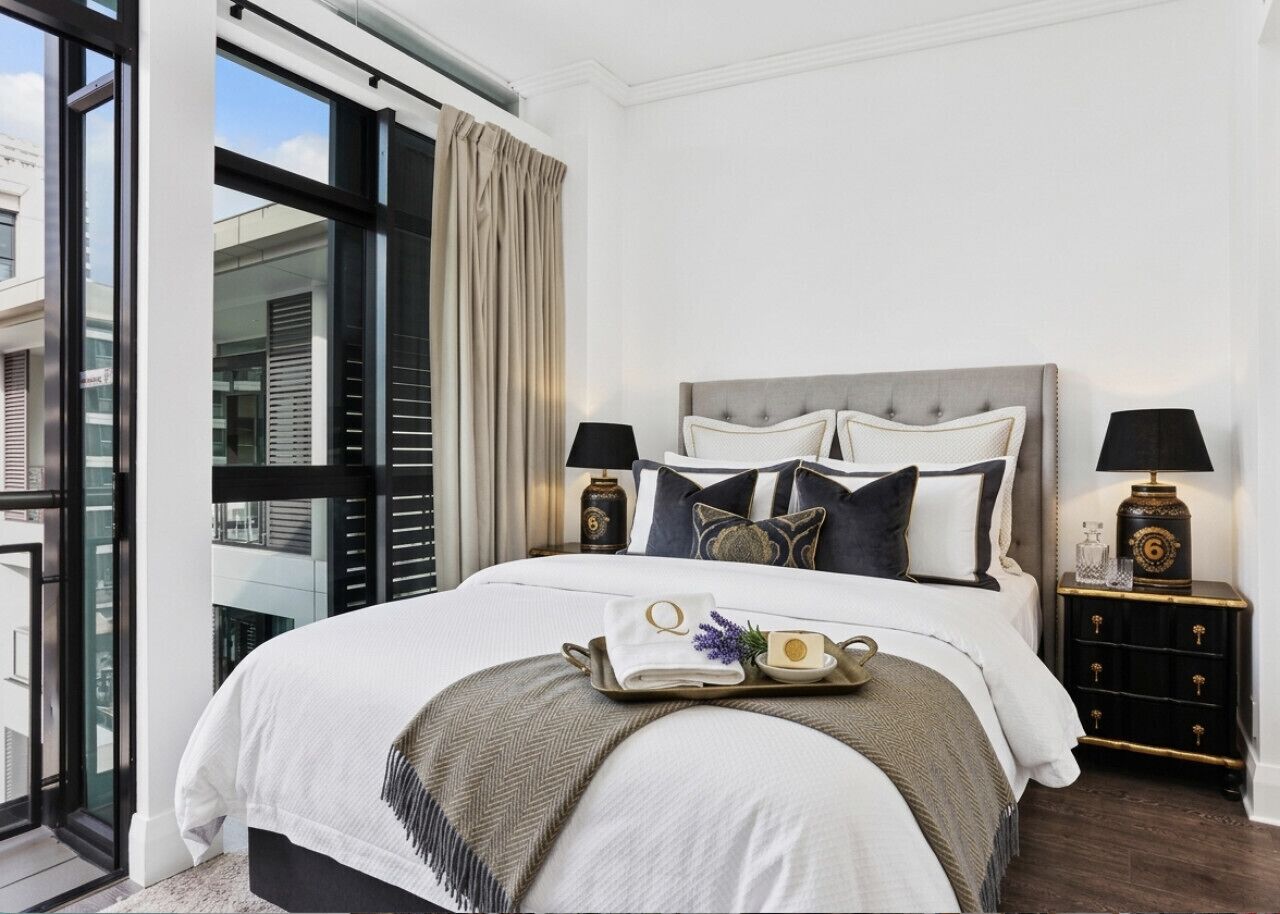 A bedroom with a large bed, two bedside tables with lamps, a tray with toiletries, and a view through a large window.