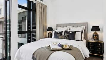 A bedroom with a large bed, two bedside tables with lamps, a tray with toiletries, and a view through a large window.