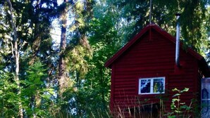 Una cabaña roja rodeada por un bosque frondoso y hierba alta.
