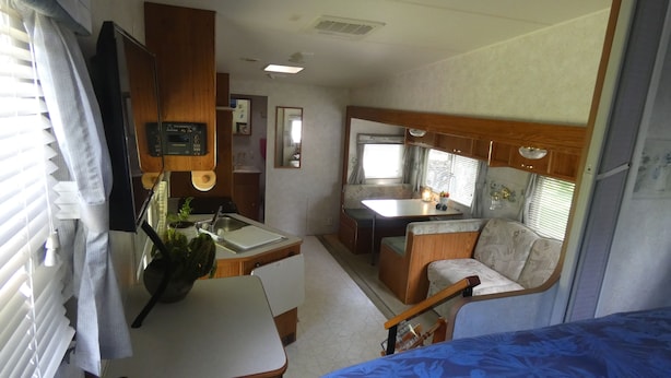 A compact RV interior with a kitchenette, a dining area, and a sleeping space.