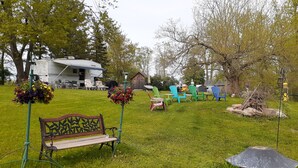 A grassy outdoor area with a wooden bench, colorful Adirondack chairs, and a small gazebo.