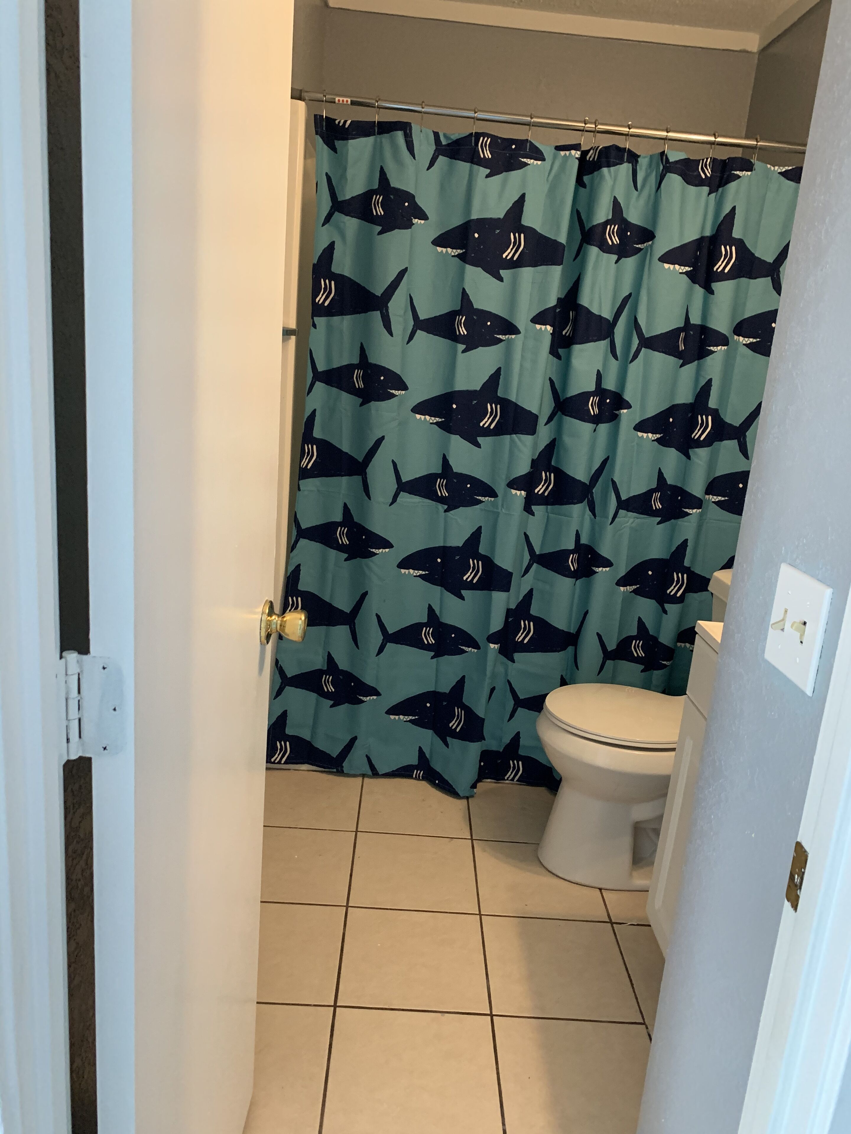 A bathroom with a toilet, a shower curtain with a shark pattern, and a tiled floor.