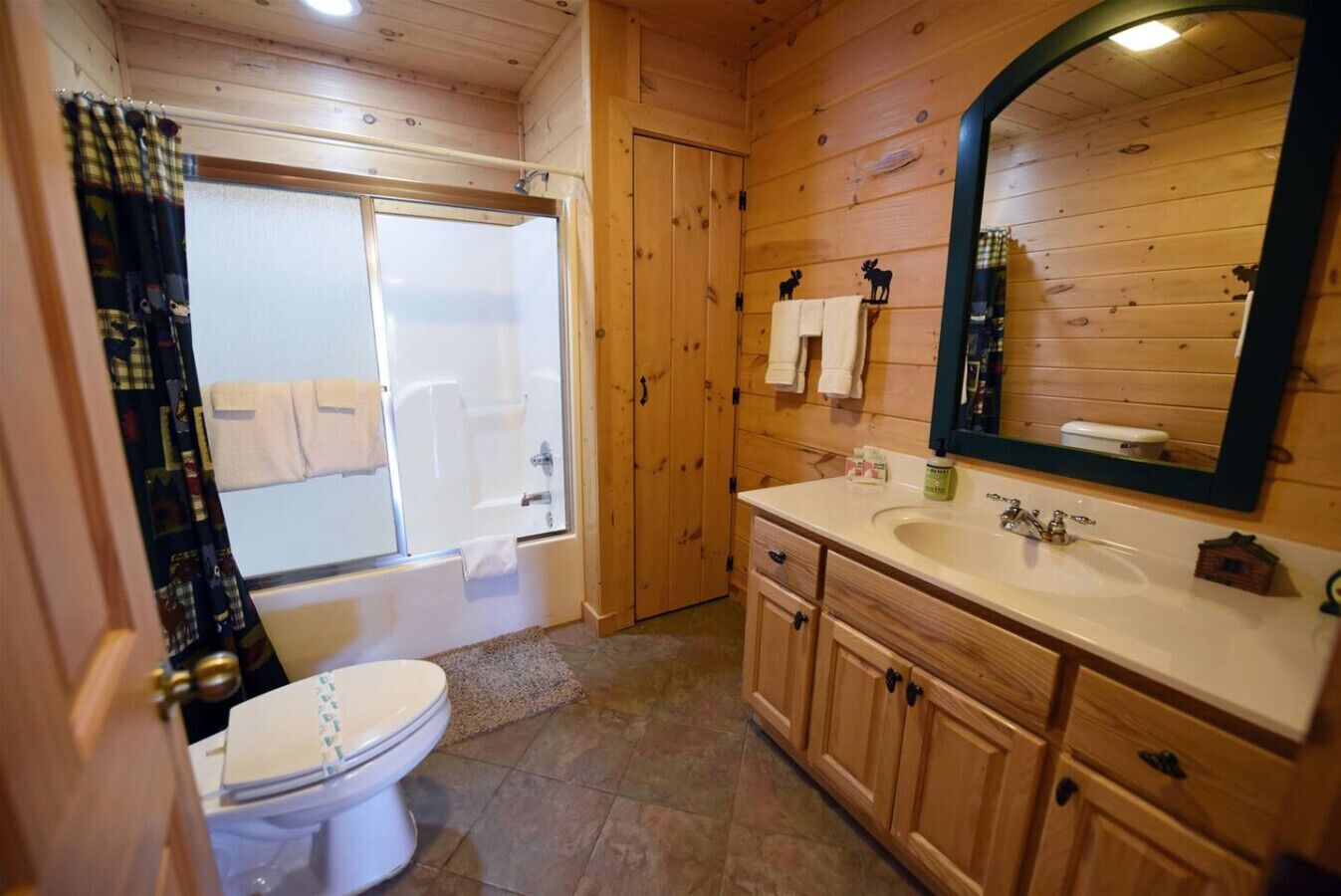 A wooden cabin bathroom with a shower, toilet, sink, and mirror.