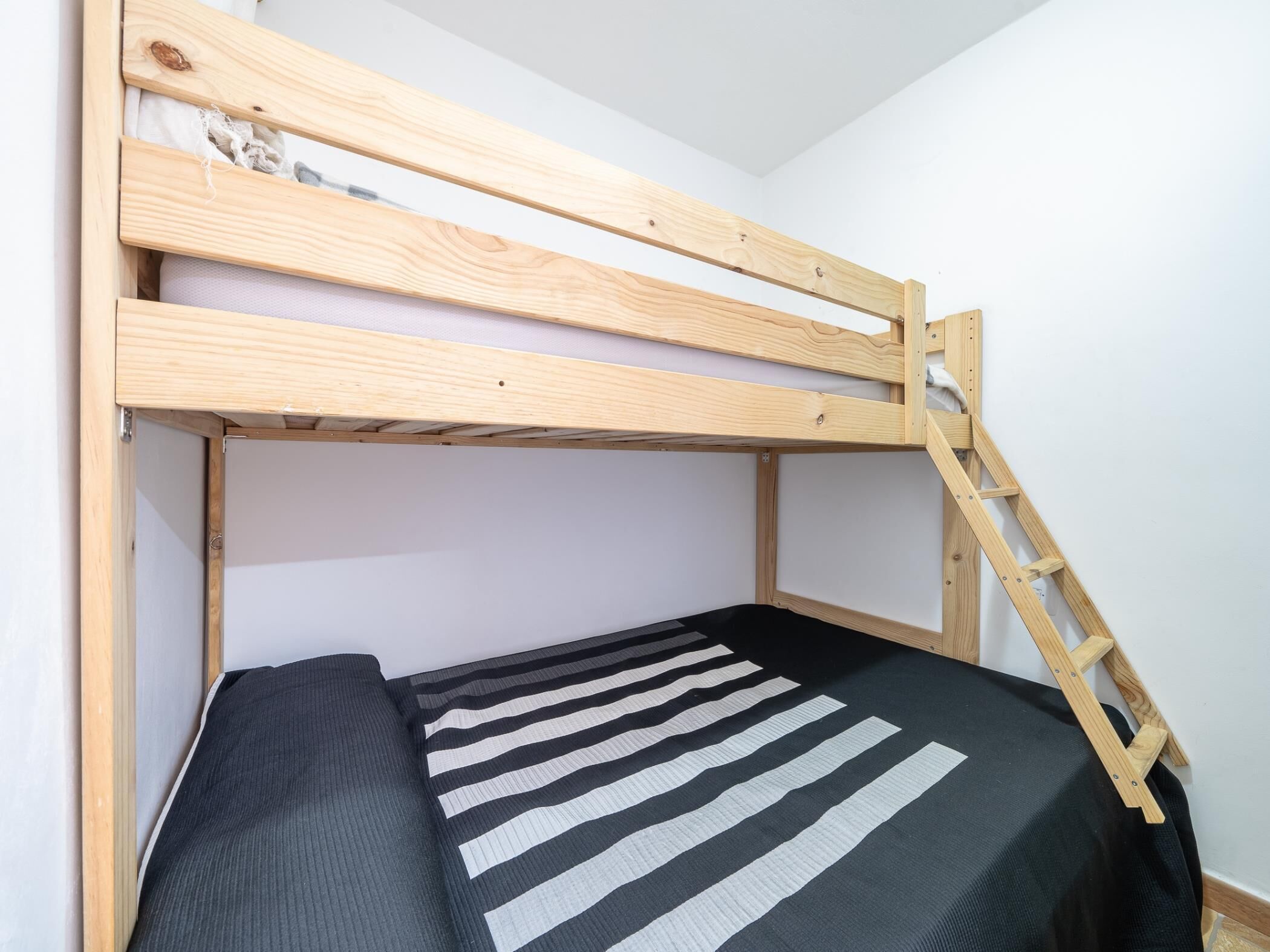 Ein Stockbett mit Holzrahmen und einer schwarz-weiß gestreiften Bettdecke.