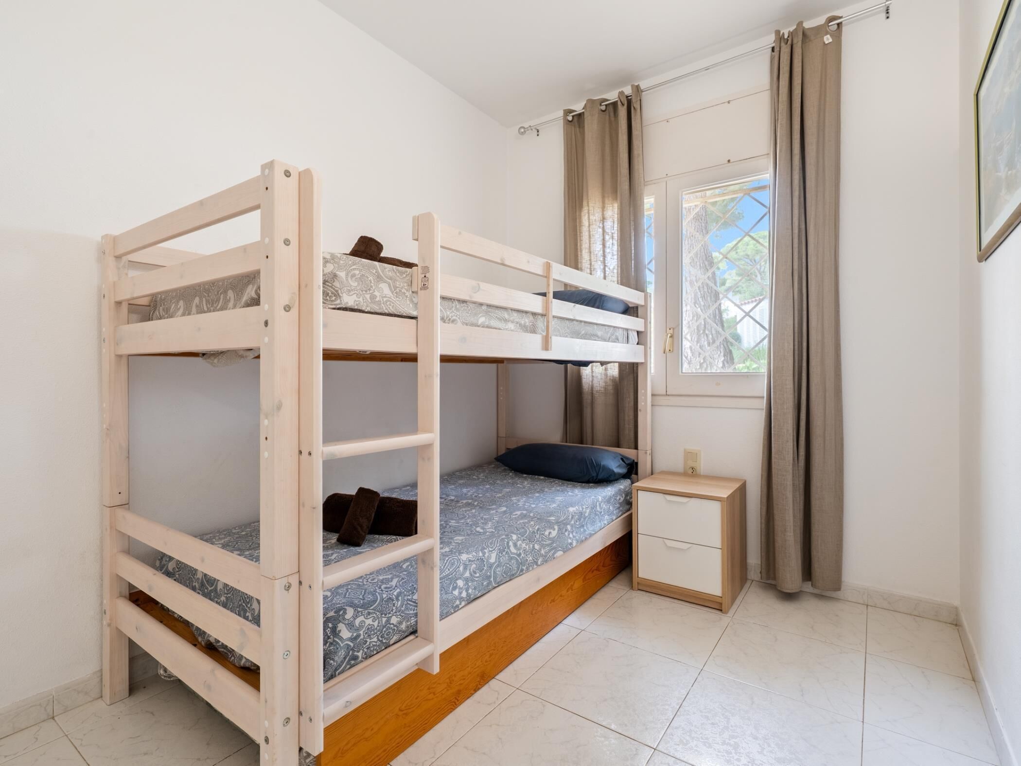 Habitación con literas, ventana, cortinas y una mesita de noche pequeña.