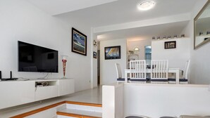 Una sala de estar moderna con un televisor de pantalla plana, muebles blancos, una escalera y un comedor.