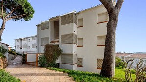 Un edificio de varios pisos con un sendero de baldosas que lleva a la entrada, rodeado de follaje y árboles.