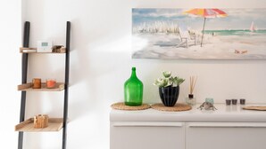 Une pièce avec une commode blanche, un tableau représentant une scène de plage et une bouteille verte posée sur la commode.