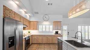 A modern kitchen with stainless steel appliances, wooden cabinets, a large window, and a clock on the wall. - Enjoy a personal beach experience! Expansive gulf side deck! - Dauphin Charm (Dauphin Island)