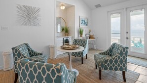 A spacious living area with a view of the ocean, featuring a round table, two patterned armchairs, a white console table, and a decorative mirror. - Enjoy a personal beach experience! Expansive gulf side deck! - Dauphin Charm (Dauphin Island)