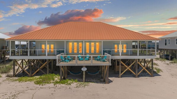 A beachfront property with a large open deck, multiple seating areas, and a covered section with windows.