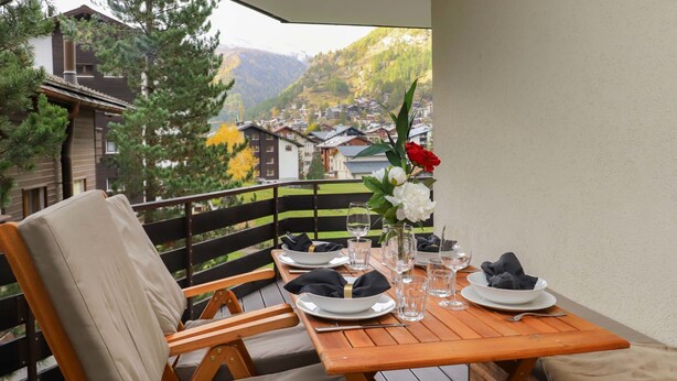 A wooden deck with a table set for two, overlooking a mountainous landscape. - Papillon by Interhome (Zermatt)