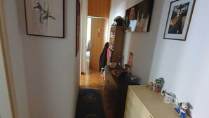 Un couloir étroit doté d’un plancher en bois, d’un tapis à motifs, d’une armoire en bois avec des tiroirs et de tableaux encadrés accrochés aux murs.